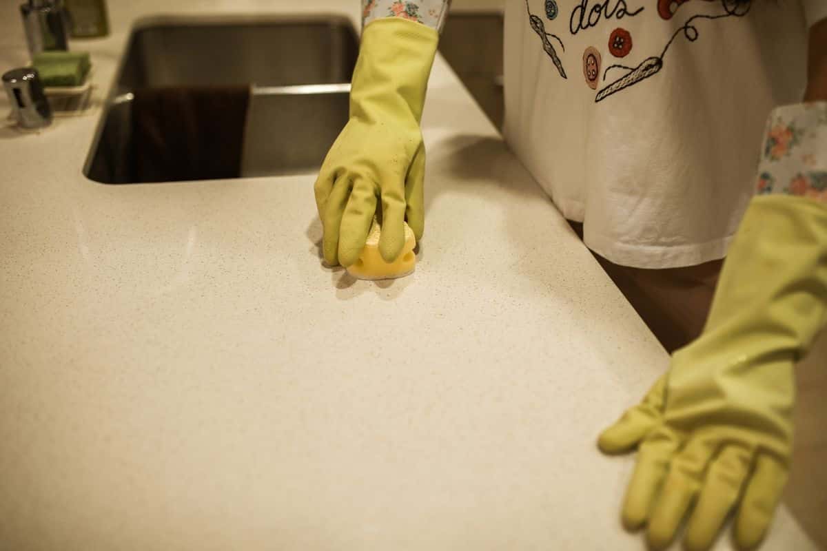 Gloved hands wiping a kitchen counter with a sponge
