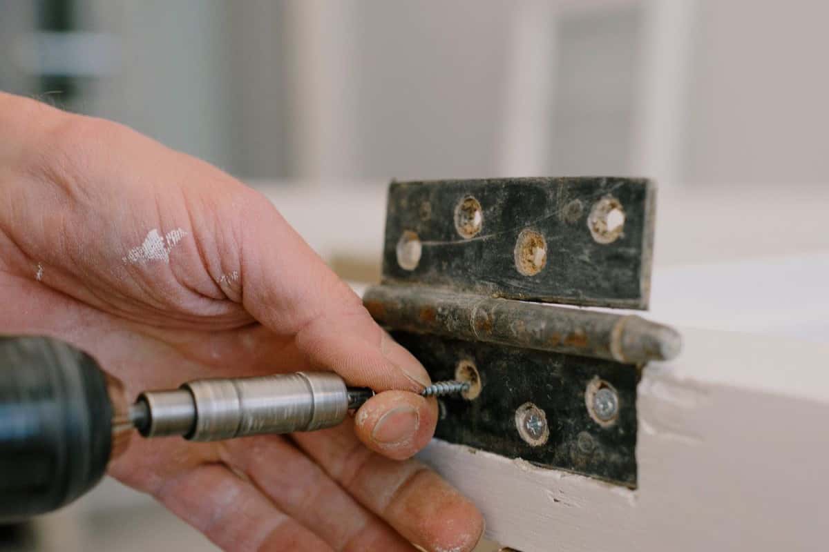 Close-up of a hinge being fixed to a door with a screwdriver