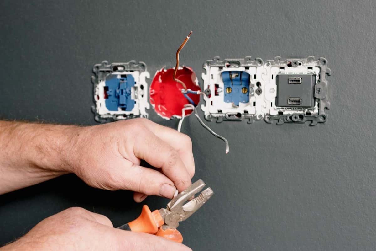 An electrician wiring a wall socket with pliers