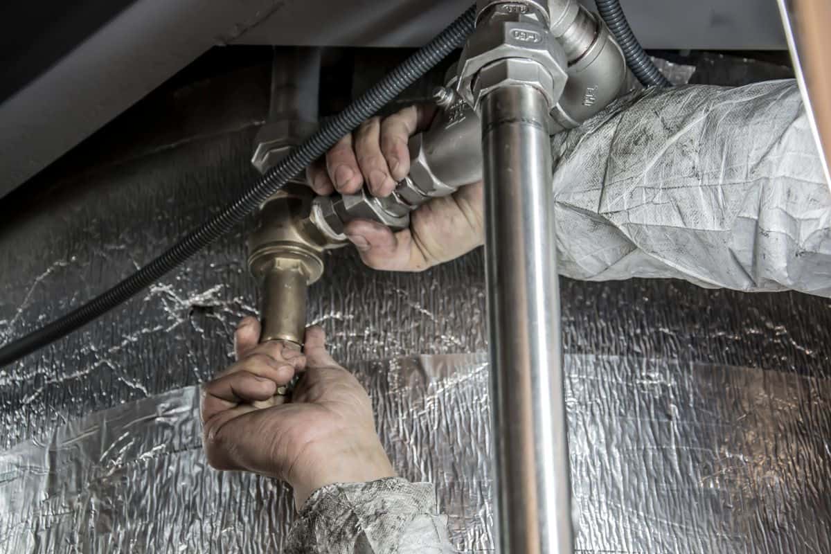 A plumber tightening pipe fittings under a sink