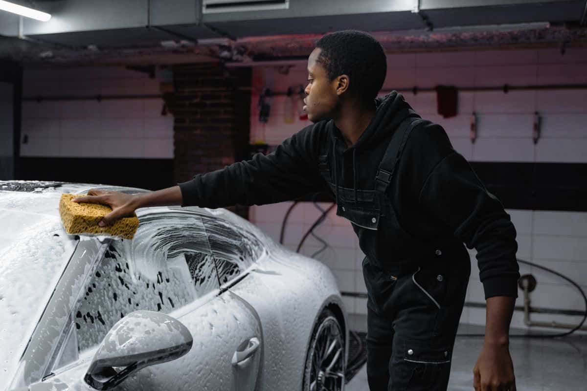 A person washing a silver car with a sponge