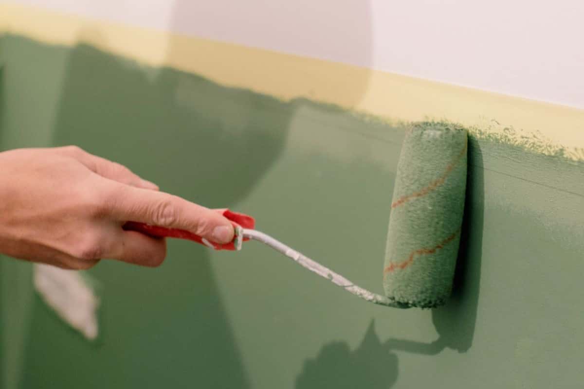 A roller applying green paint to an interior wall