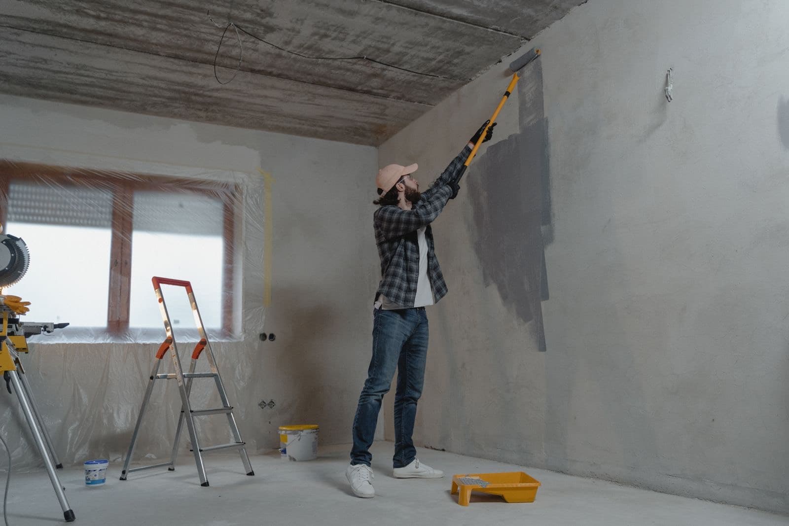 A person on a stepladder painting the wall of an empty room