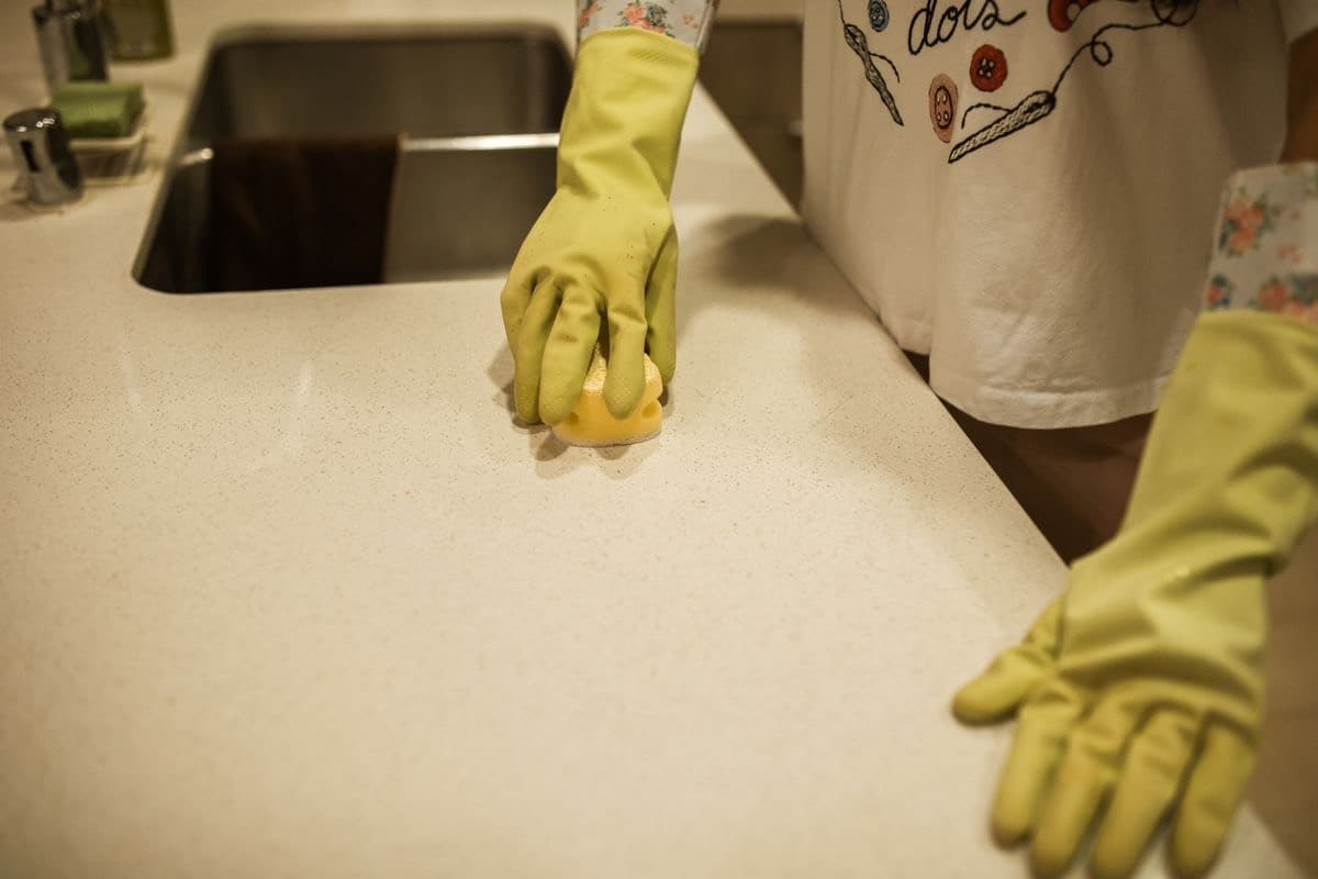 Gloved hands wiping a kitchen counter with a sponge