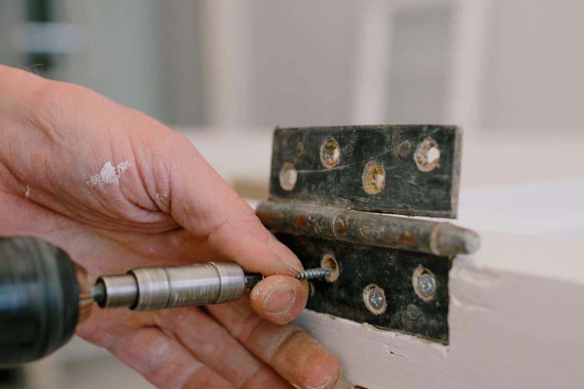 Close-up of a hinge being fixed to a door with a screwdriver