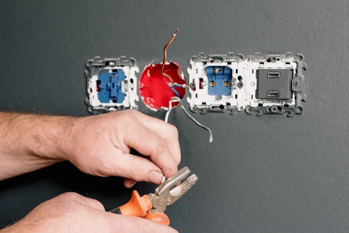 An electrician wiring a wall socket with pliers