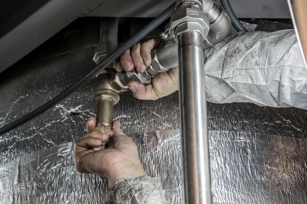 A plumber tightening pipe fittings under a sink