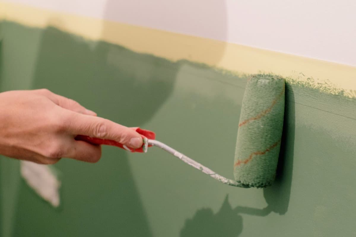 A roller applying green paint to an interior wall
