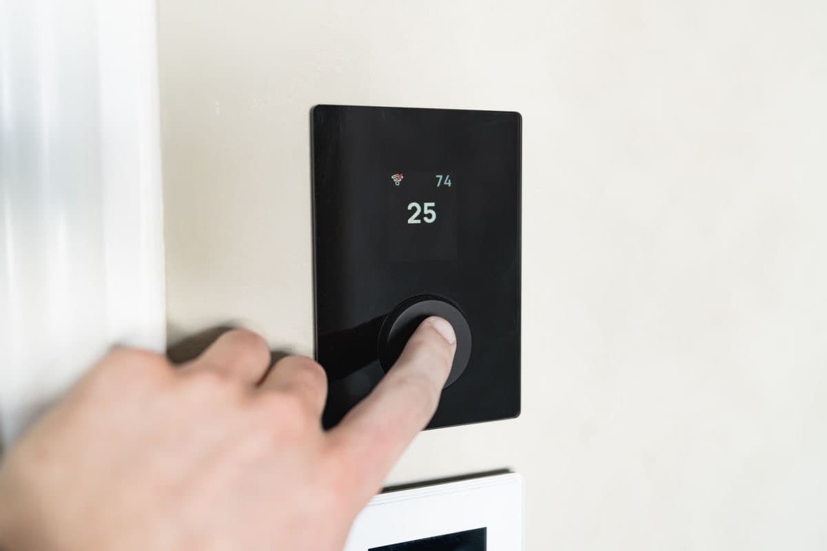 A hand adjusting a smart thermostat on a wall